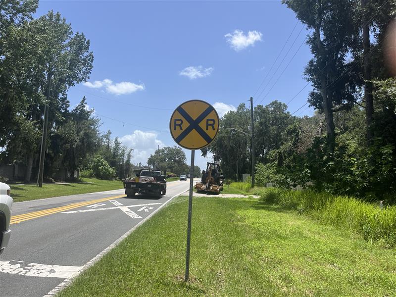 Railroad crossing sign beside road with vehicles and construction equipment nearby in Ocala.