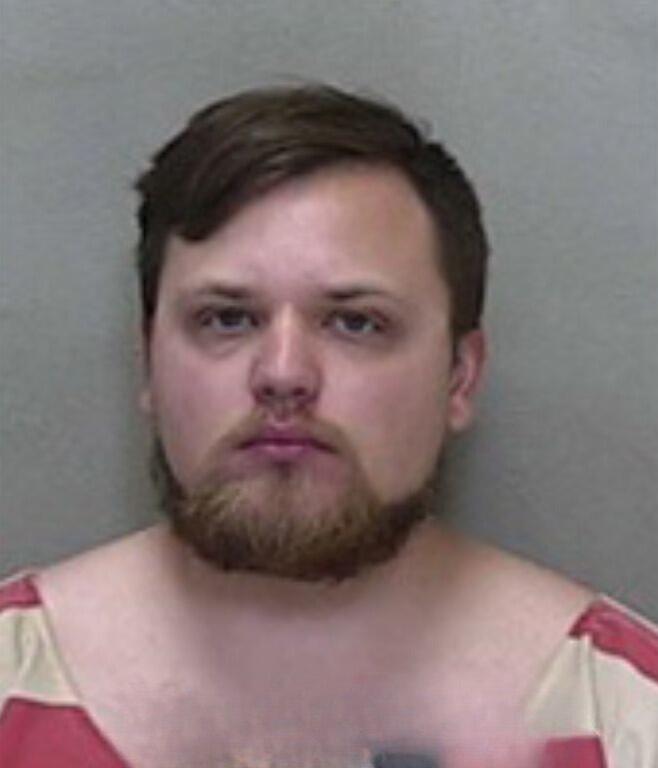 Mugshot of a man with shoulder-length hair and no visible facial hair, wearing a red-and-white striped jail uniform.