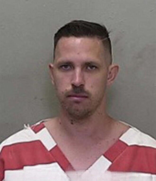 Mugshot of a man with short hair and a trimmed beard, wearing a red-and-white striped jail uniform.