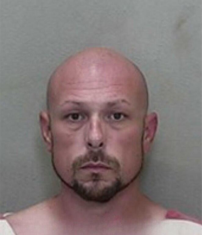 Mugshot of a bald man with a beard, wearing a red-and-white striped jail uniform.