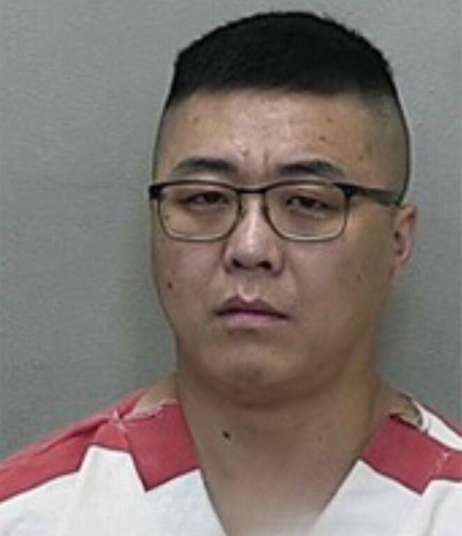 Mugshot of a man with short black hair and glasses, wearing a red-and-white striped jail uniform.