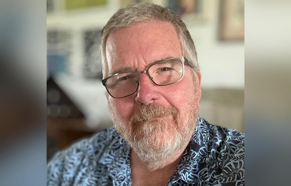 Portrait of Larry Whitler, smiling slightly and wearing glasses and a patterned shirt