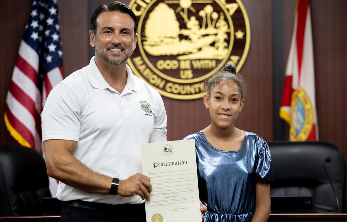 Mayor Ben Marciano and Isabella Fipps smile while holding a proclamation at Ocala City Hall.