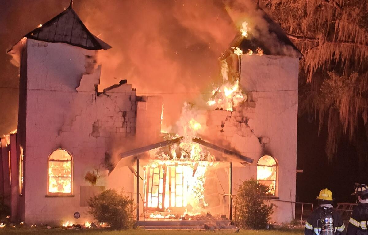 Flames consume the front of Antioch Missionary Baptist Church as firefighters look on during early morning fire.