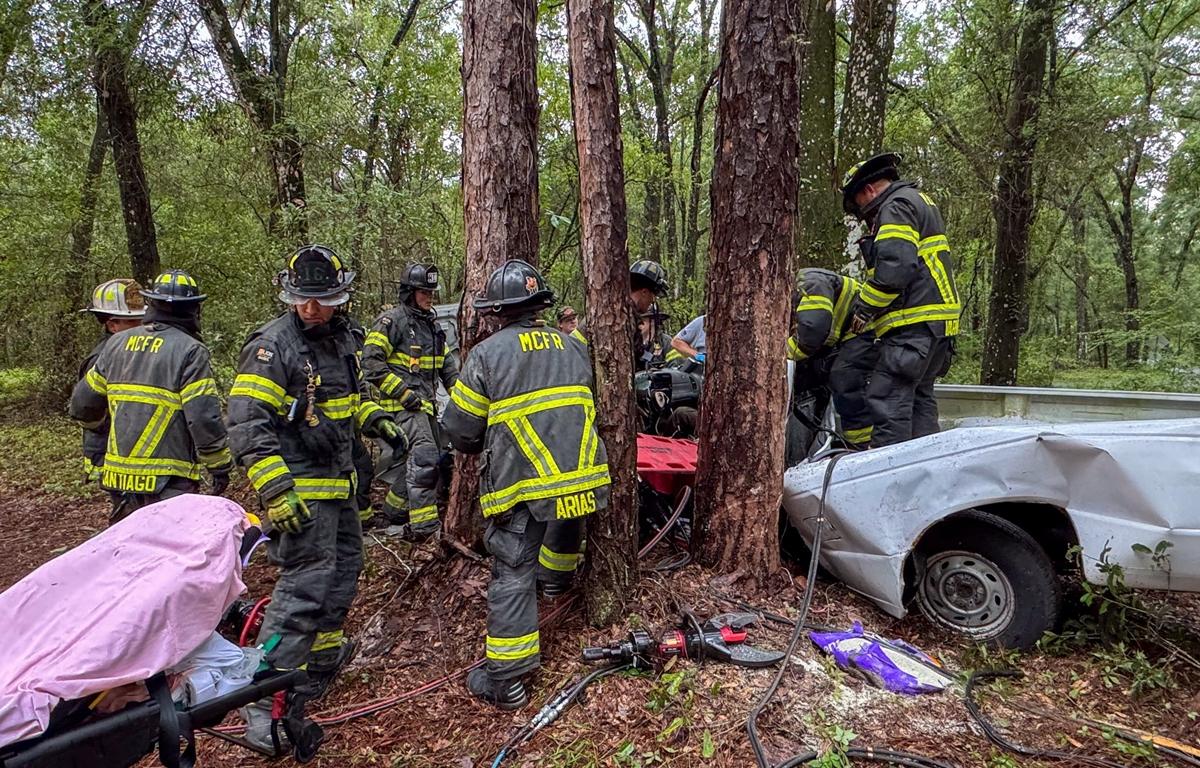 Firefighters surrounding crashed truck in wooded area during vehicle extrication.