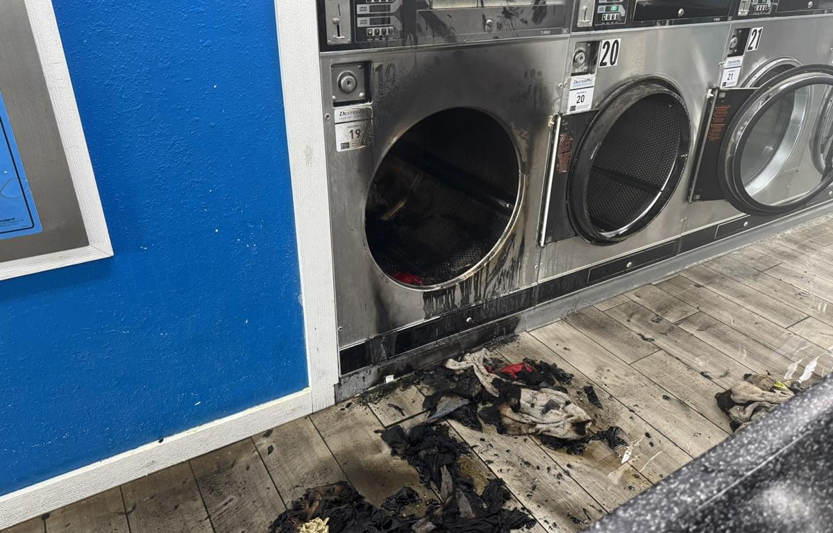 Close-up of a burnt dryer with charred laundry and smoke damage at a laundromat.