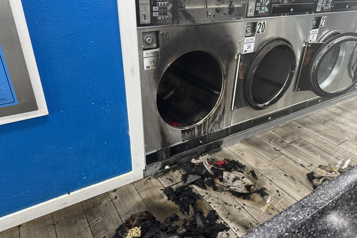 Close-up of a burnt dryer with charred laundry and smoke damage at a laundromat.