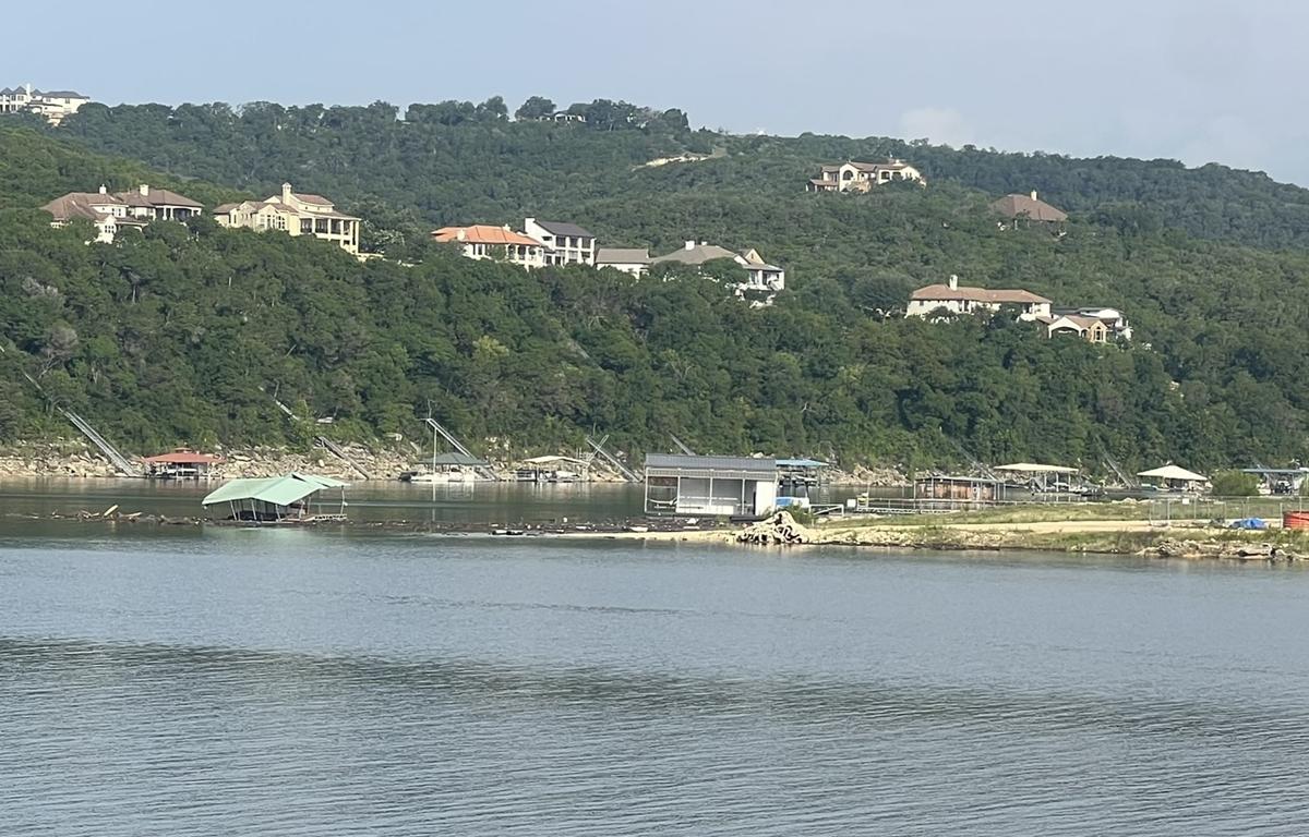 Flood-damaged docks partially underwater in Lake Travis with hillside homes in background