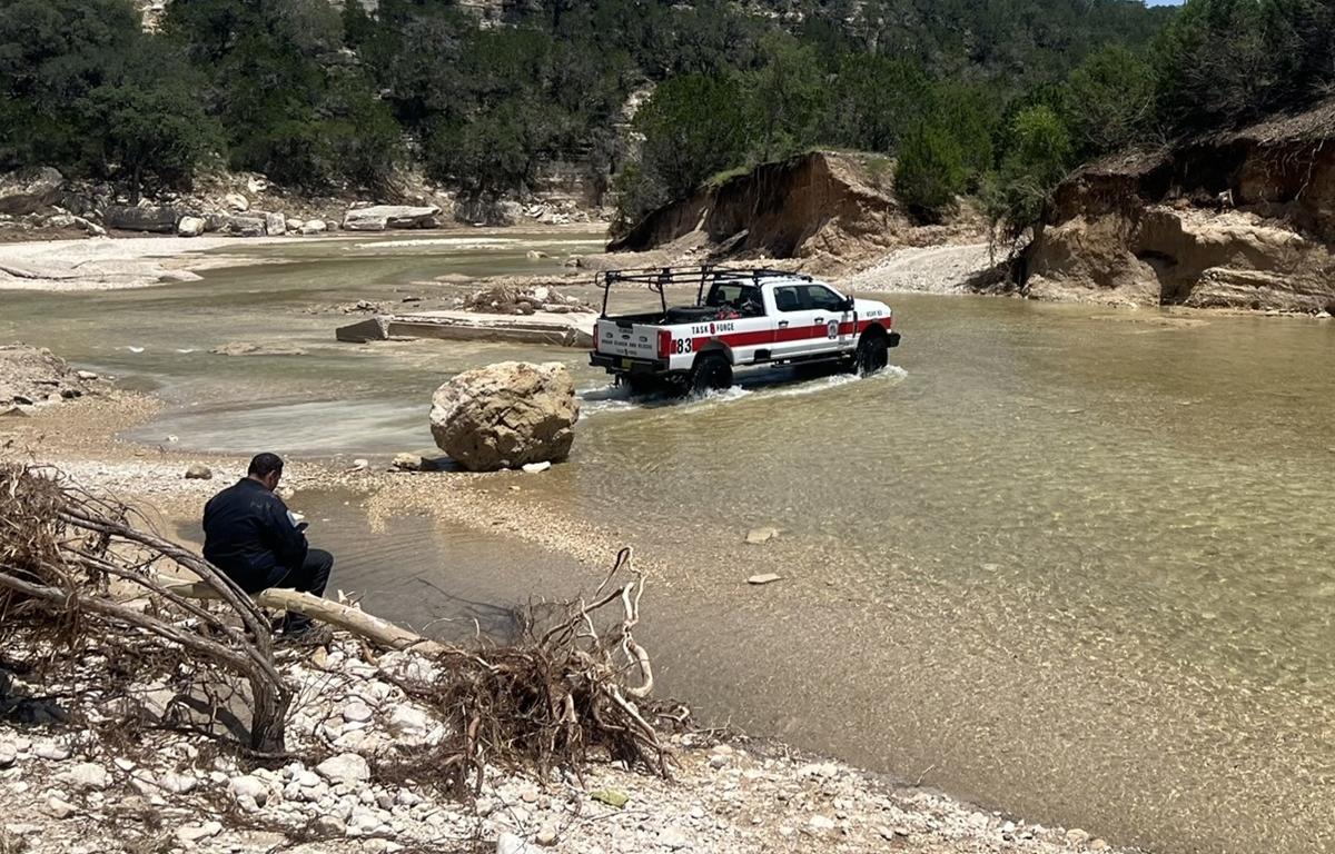 Task Force 8 vehicle drives through flooded creek while team member monitors from shore