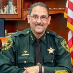 Marion County Sheriff Billy Woods seated at his desk in uniform with American flag