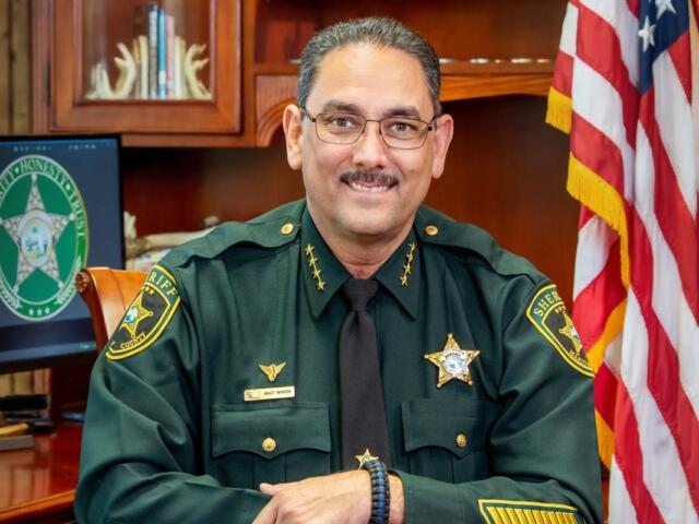 Marion County Sheriff Billy Woods seated at his desk in uniform with American flag