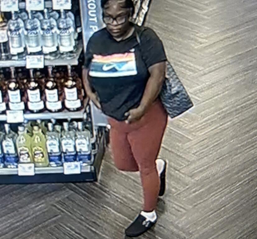 Surveillance photo of a woman wearing a black shirt and red pants inside a liquor store.
