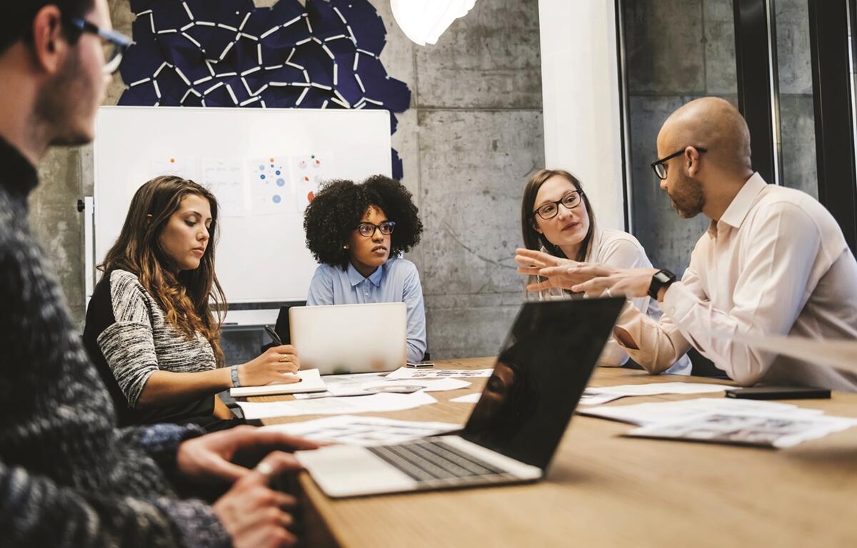 Group of marketing professionals having a team discussion around a conference table with laptops and charts.