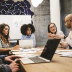 Group of marketing professionals having a team discussion around a conference table with laptops and charts.