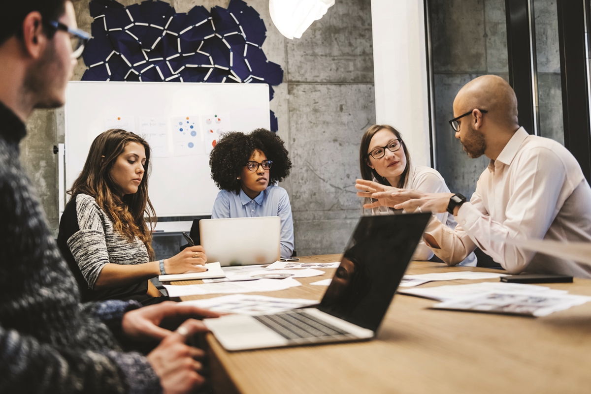 Group of marketing professionals having a team discussion around a conference table with laptops and charts.