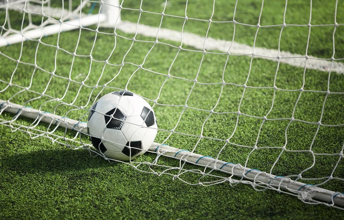Soccer ball in goal net on green turf field.