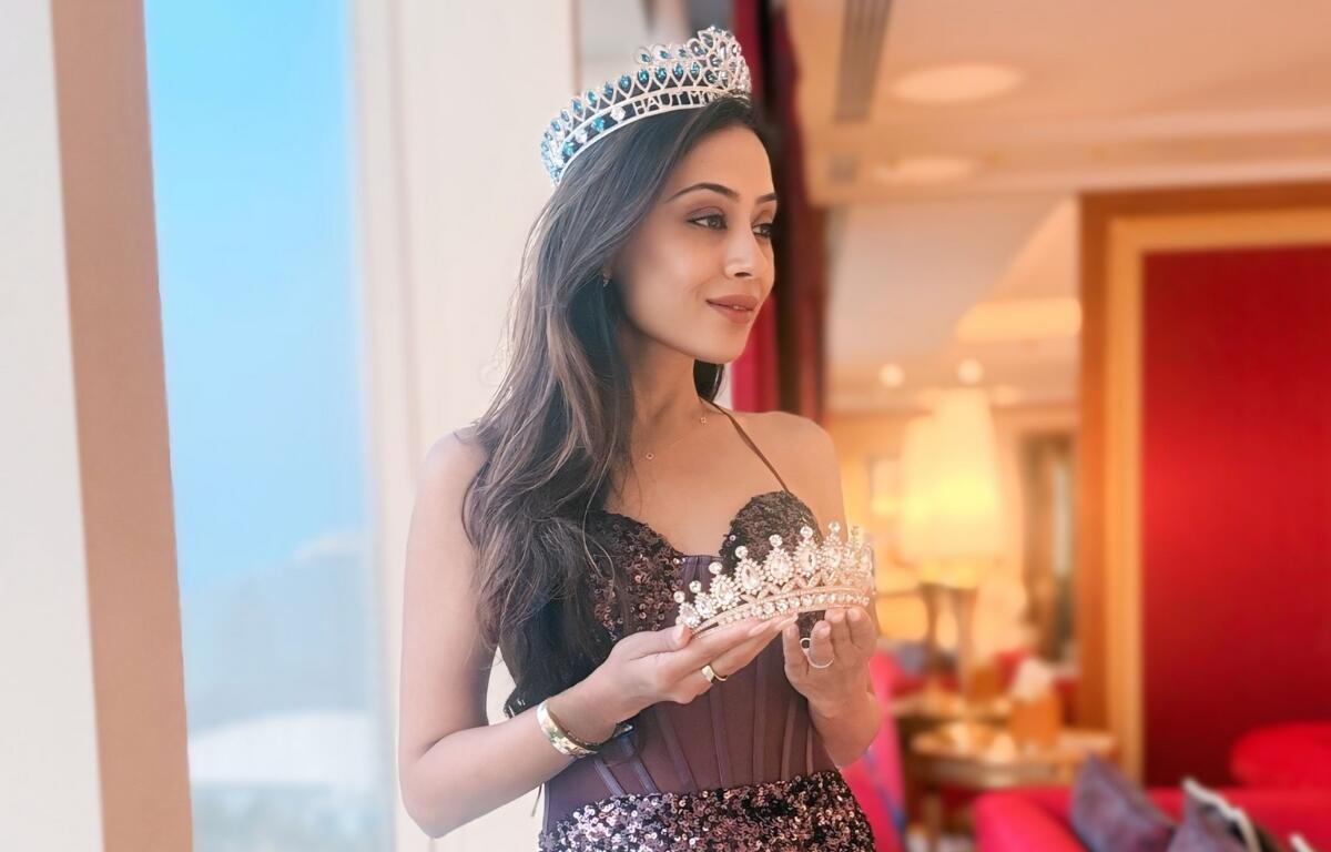 Nilam Patel wearing a crown and holding another in a hotel suite after Mrs. India Worldwide pageant in Dubai.