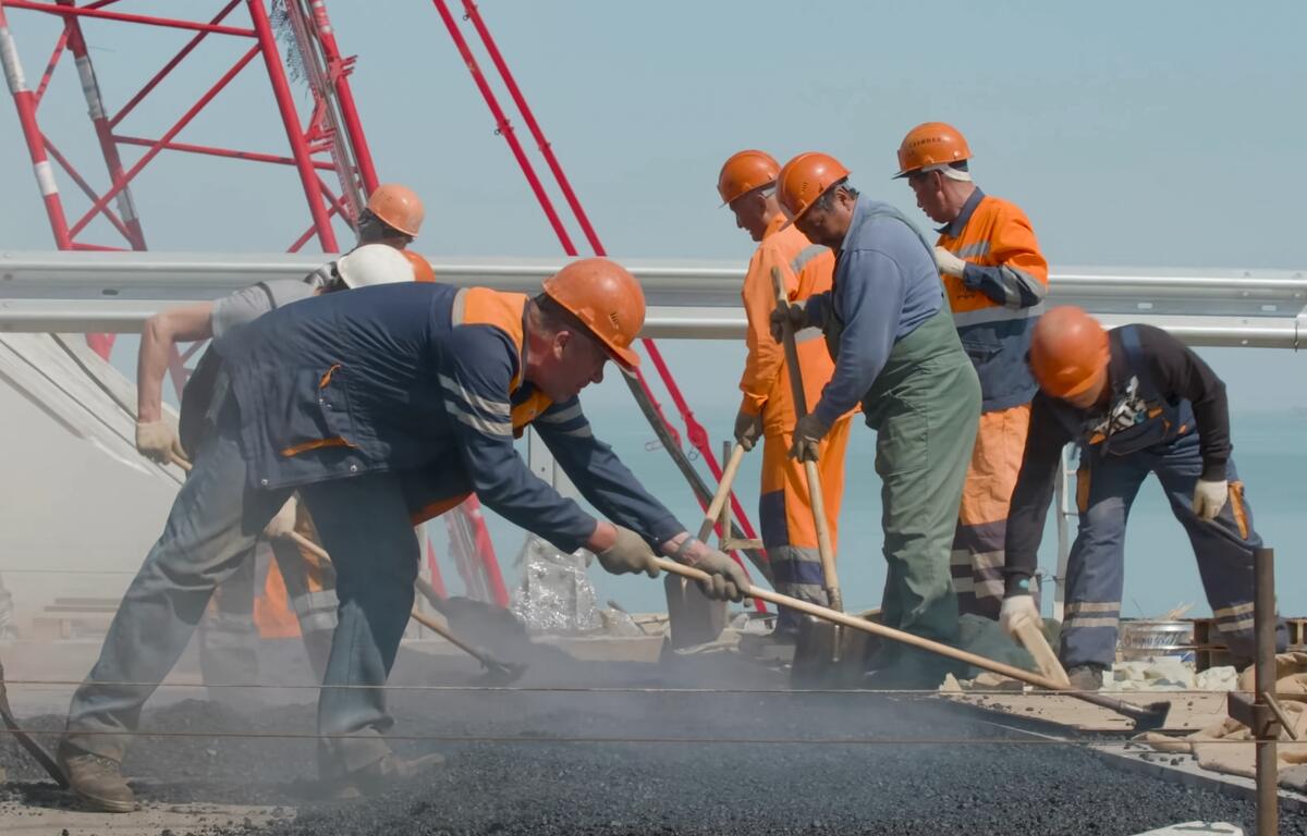 Workers in hard hats repave a road with asphalt during a construction project.