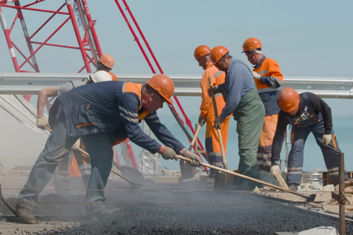 Workers in hard hats repave a road with asphalt during a construction project.
