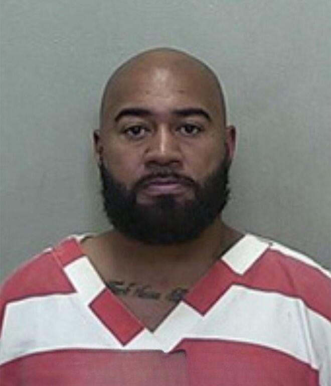 Mugshot of a bald man with a short beard, wearing a red-and-white striped jail uniform.