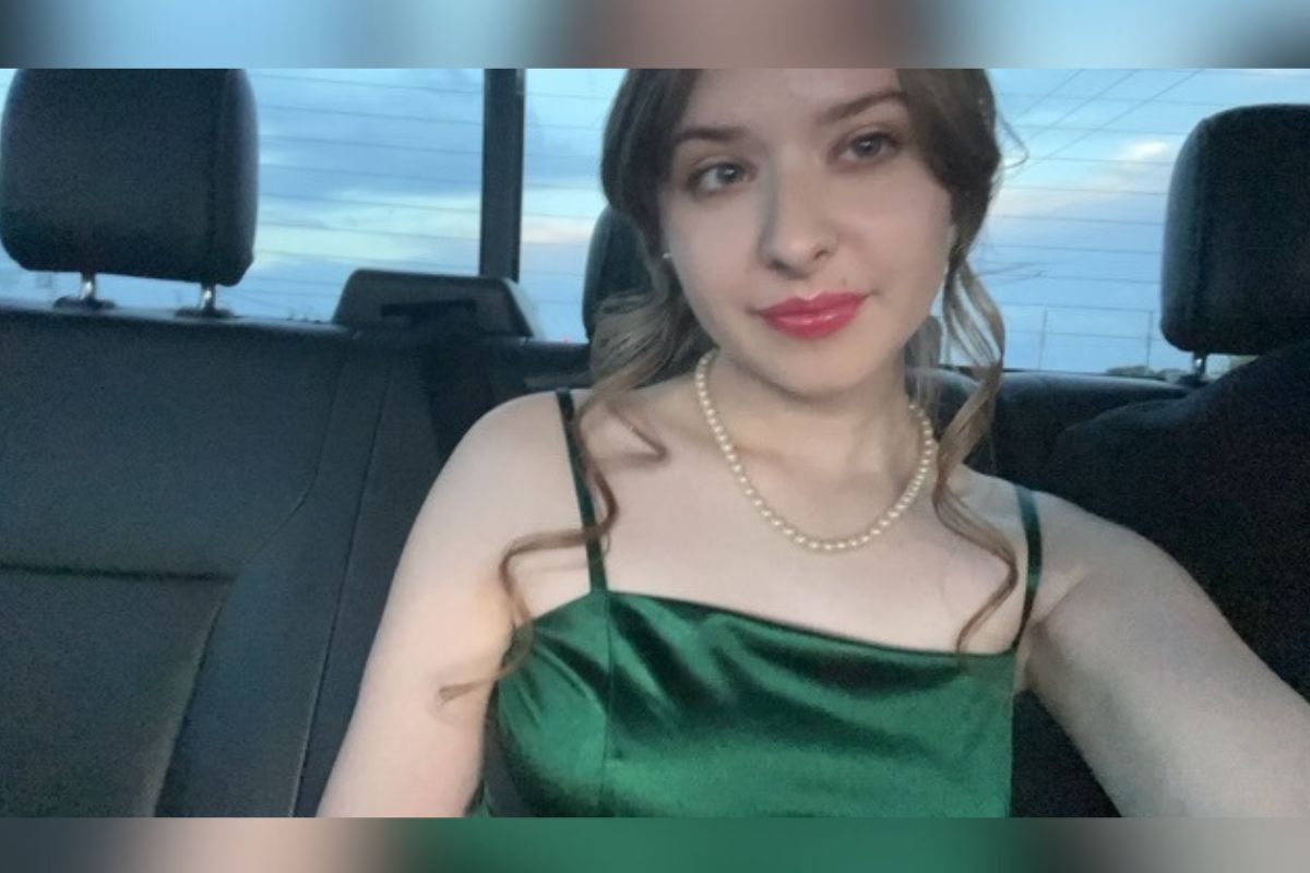 Scarlett Phillips sits in a vehicle wearing a green dress and pearl necklace, smiling at the camera.