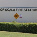 Extreme close-up of a beige building with green bushes in front of it and bold letters that read, "City of Ocala Fire Station #4." Toward the bottom of the letters is a yellow diamond-shaped sign that reads, "Safe Place." To the left of that sign is a red and white sign.