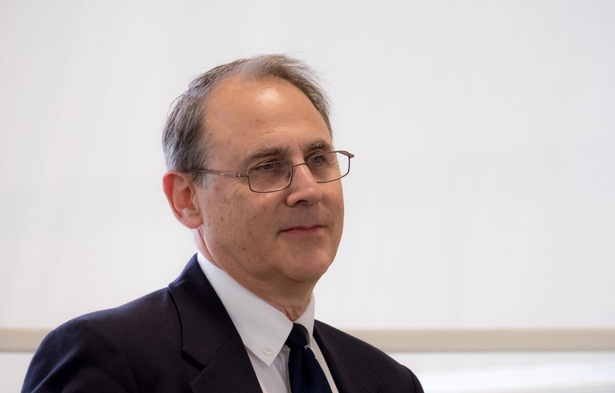 Eliot Kleinberg wearing glasses and a suit speaks during a lecture.