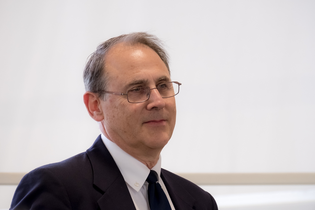 Eliot Kleinberg wearing glasses and a suit speaks during a lecture.