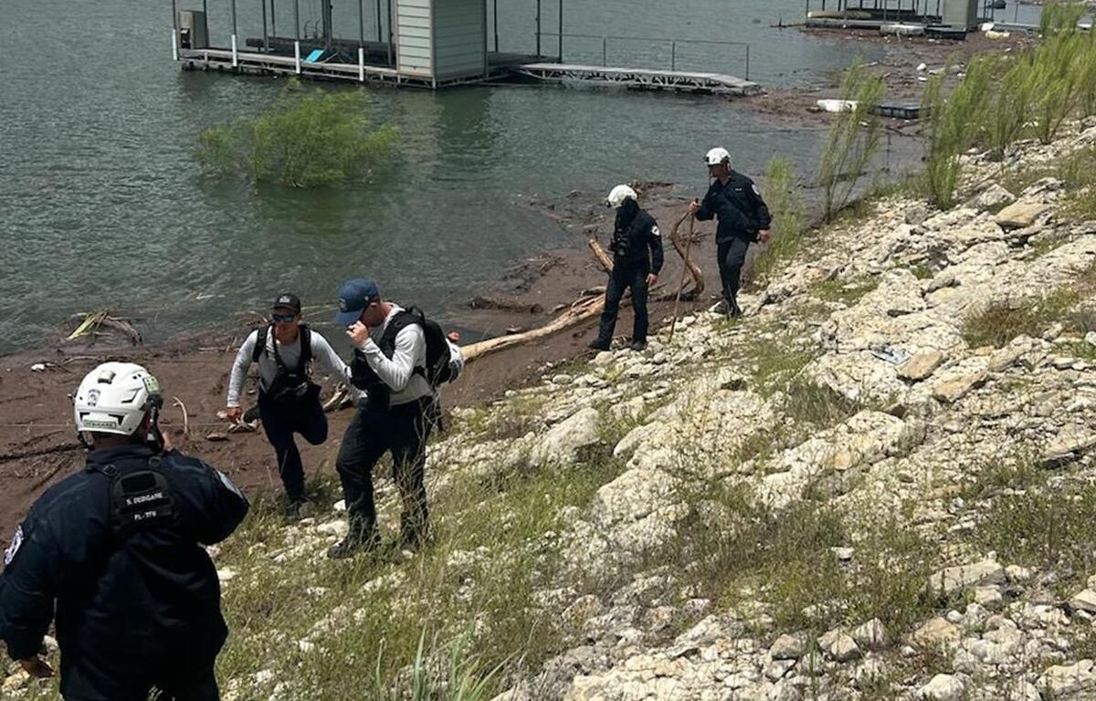 Rescue team members climb up a rocky slope from the shoreline at Lake Travis during flood response in Texas.