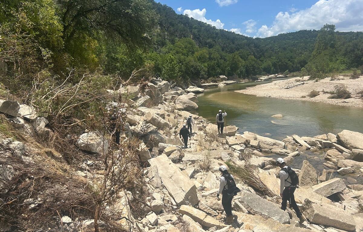 Task Force 8 personnel walking over large rocks beside a creek during flood search operations in Texas.