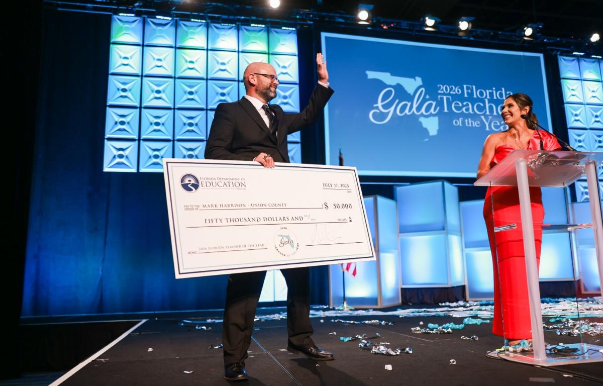 Mark Harrison holds oversized check on stage after winning 2026 Florida Teacher of the Year award.