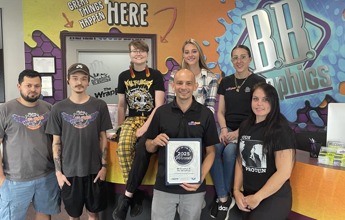BB Graphics and The WrapPros team members pose in front of their logo with a framed 2025 Best of the 352 award.