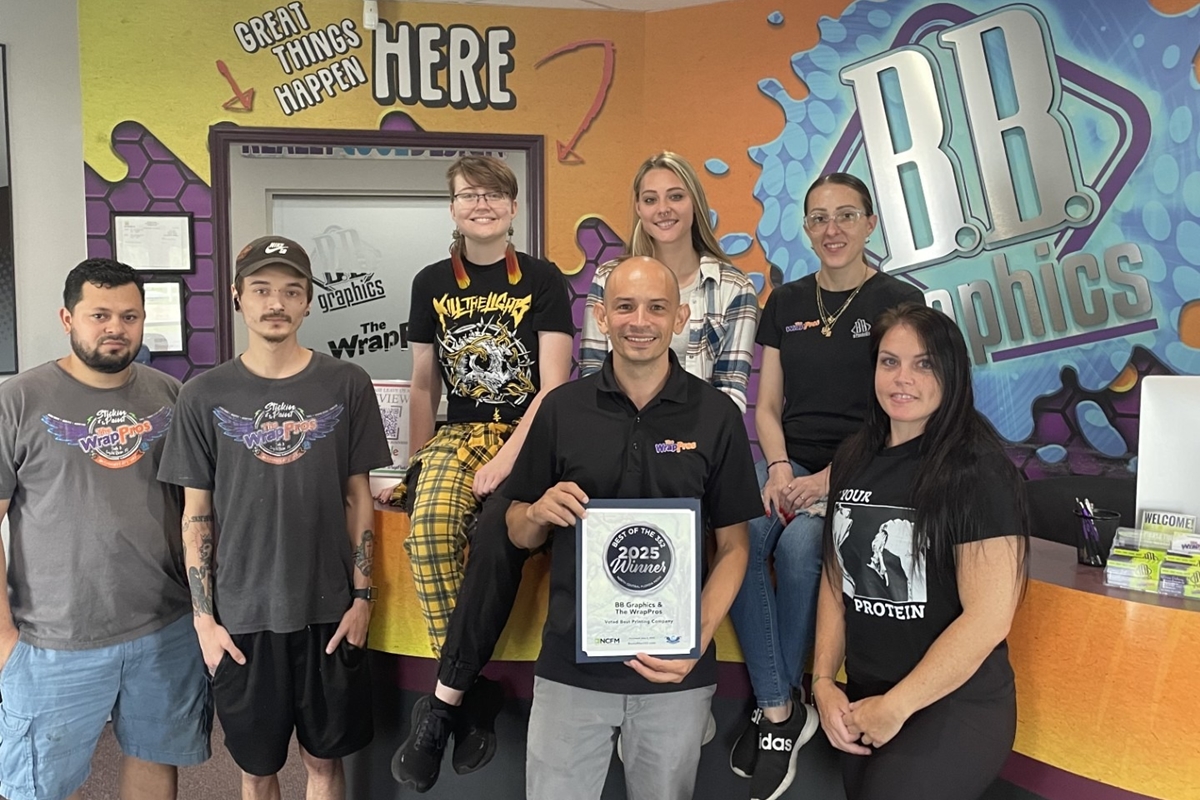 BB Graphics and The WrapPros team members pose in front of their logo with a framed 2025 Best of the 352 award.