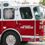Close-up of a red fire truck with "Marion Country Fire Rescue" and "24" written on the side with a tree and light sky in the background.
