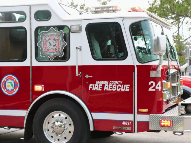 Close-up of a red fire truck with "Marion Country Fire Rescue" and "24" written on the side with a tree and light sky in the background.