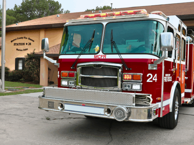 Front of a fire truck with "MCRF" written on the front with "24" and "Marion County Fire Rescue" on the side. A peach-colored fire station is in the background with "Marion County Fire Rescue Station # 24 Marion Oaks" written on the building to the left and flag pole to the left.