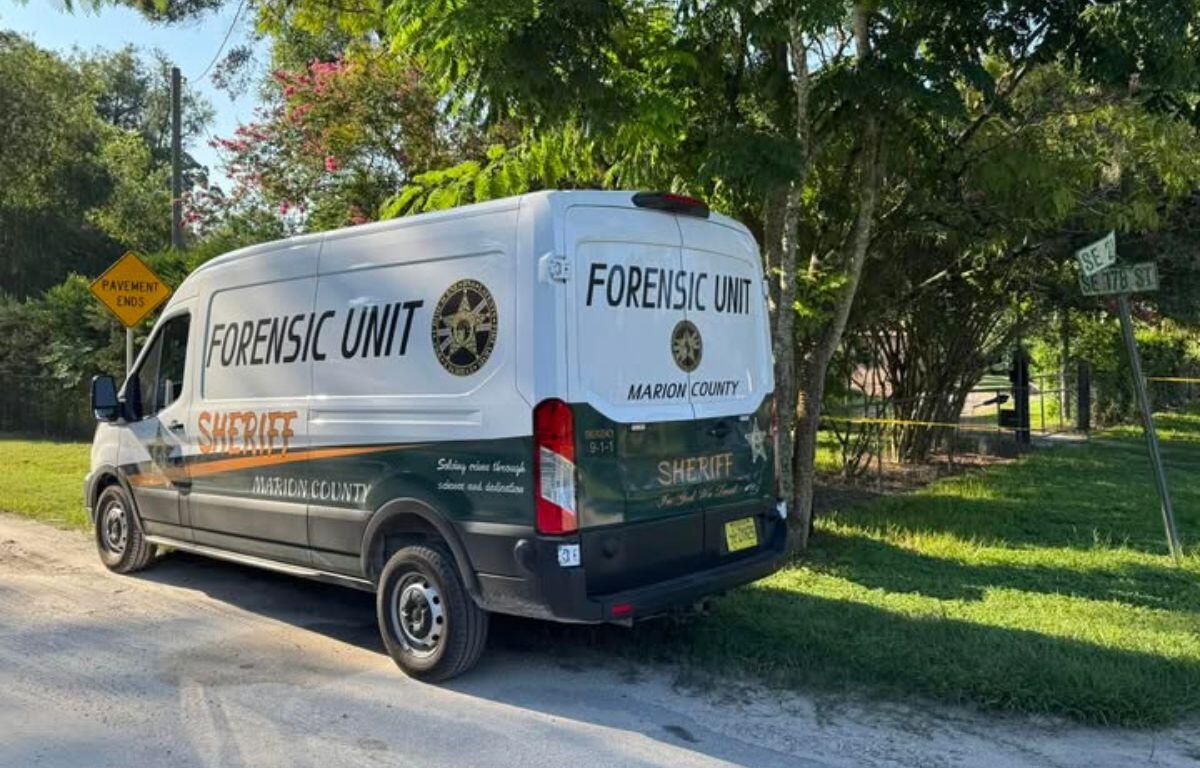 A Marion County Sheriff's Office Forensic Unit van is parked on a rural roadside near a street sign for SE 17th Street and SE 17th Court. Yellow crime scene tape is visible in the background, partially enclosing a tree-shaded area. A "Pavement Ends" road sign stands nearby, indicating the transition from paved to unpaved road.