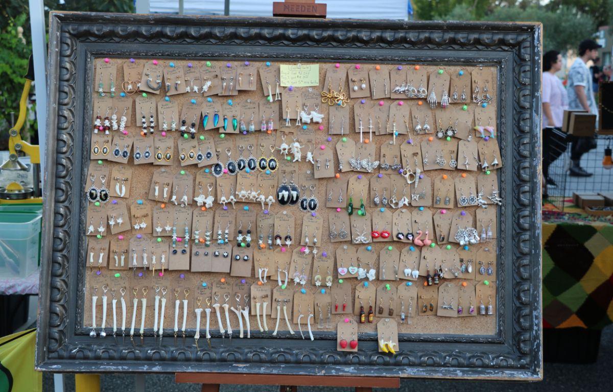 A framed display board covered with rows of unique, handcrafted earrings arranged neatly.