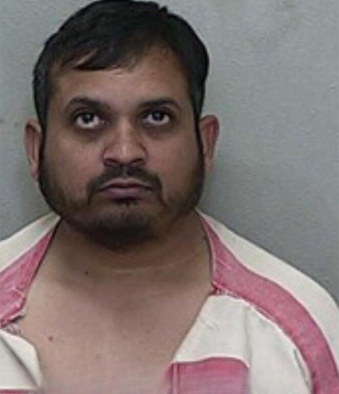 Mugshot of a man with short dark hair and facial hair, wearing a red-and-white striped jail uniform.