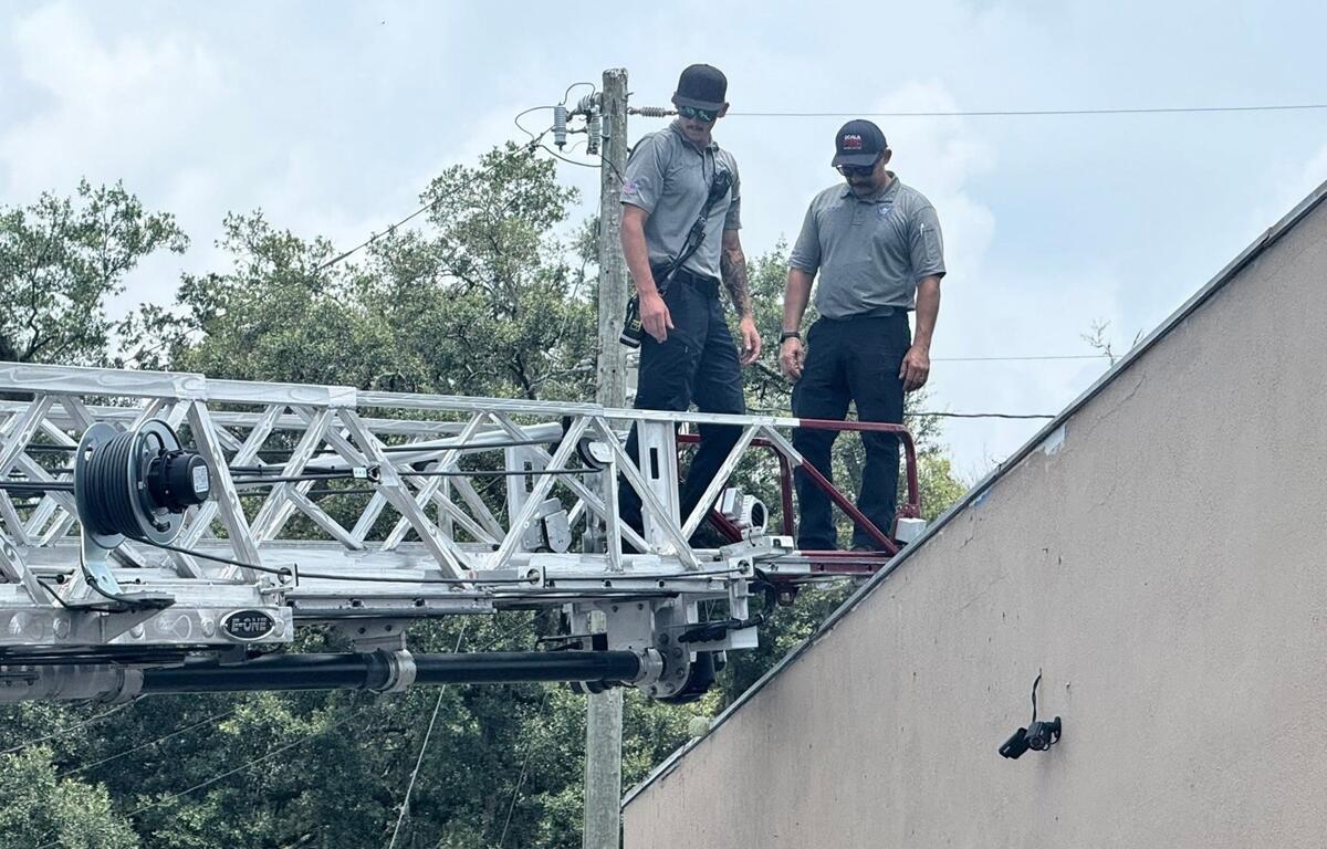 Two Ocala firefighters standing on ladder truck platform near rooftop during training