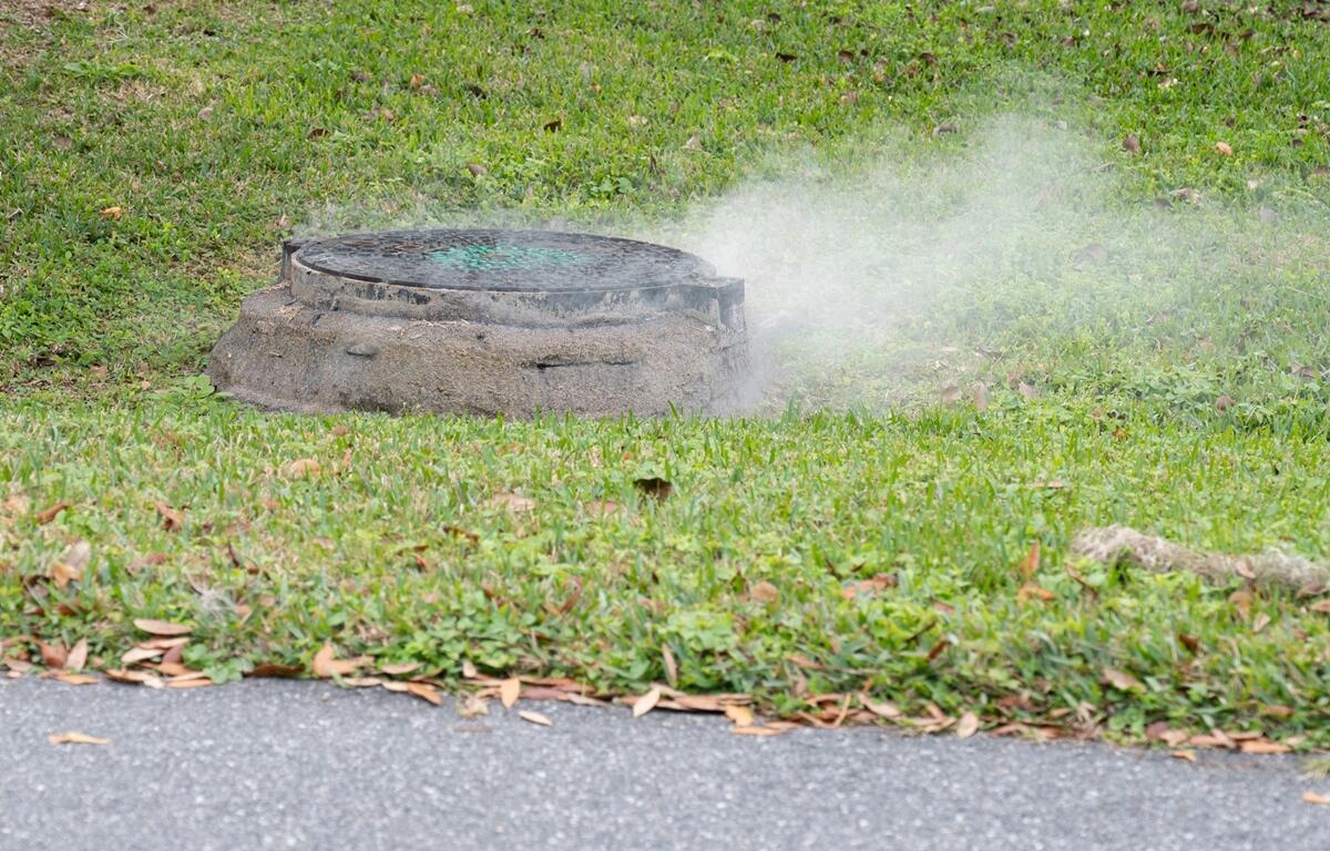 Smoke coming out of a manhole cover in grassy area during utility testing
