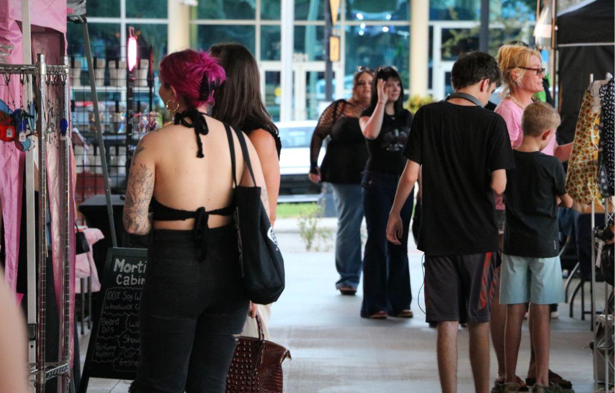 A crowd of people walking between vendor booths at an outdoor marketplace.