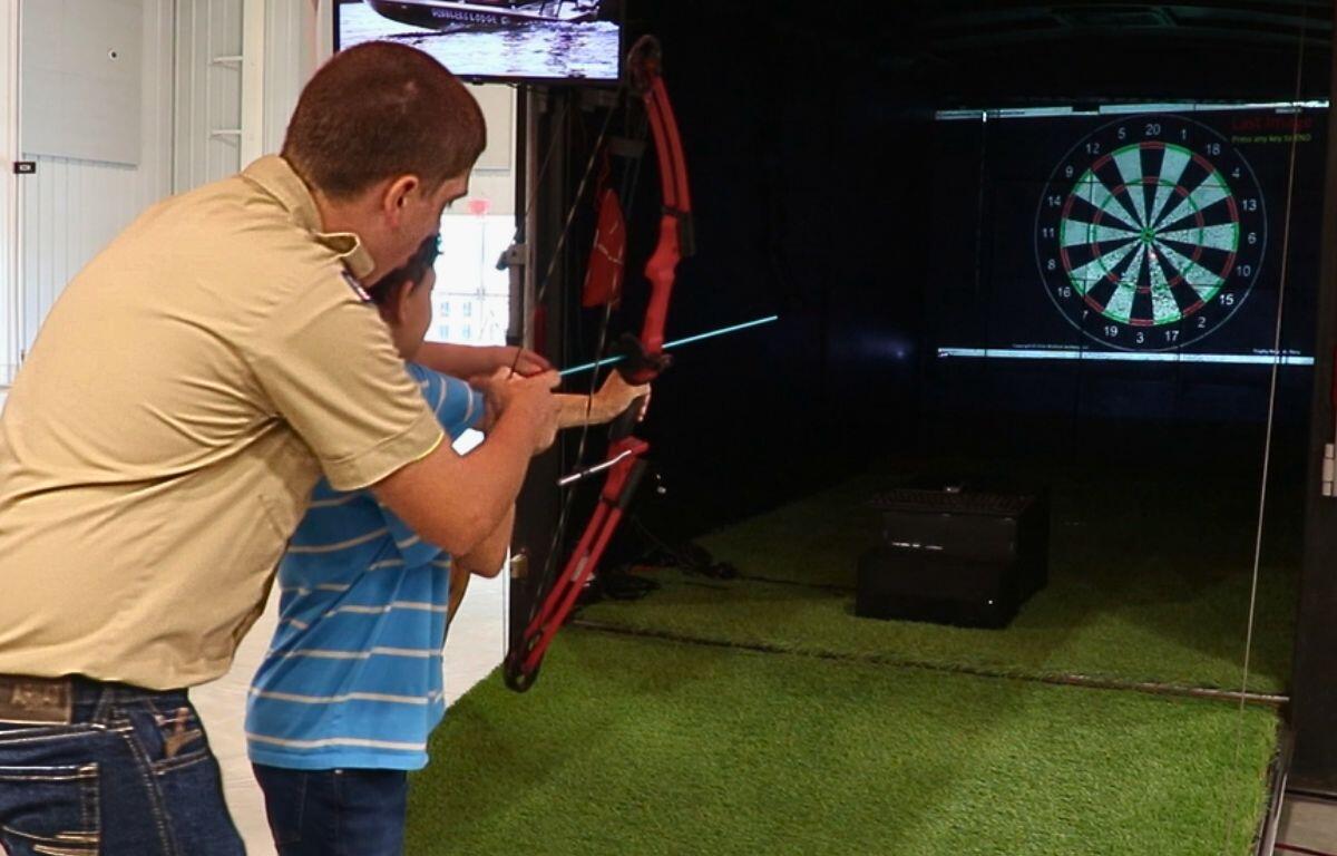 Attendee aiming a bow at a digital archery target inside the expo activity area.
