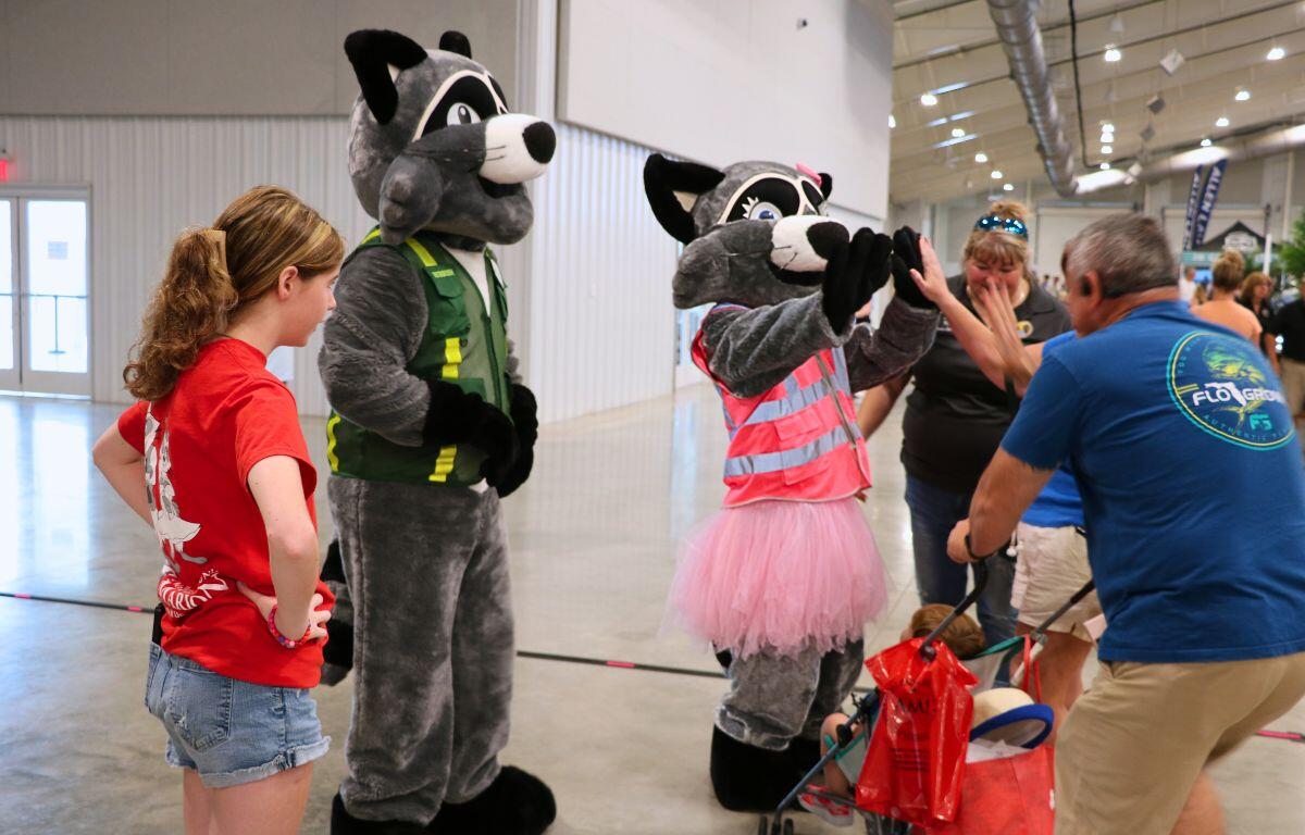Two costumed racoon mascots in construction vests greeting a group of people.