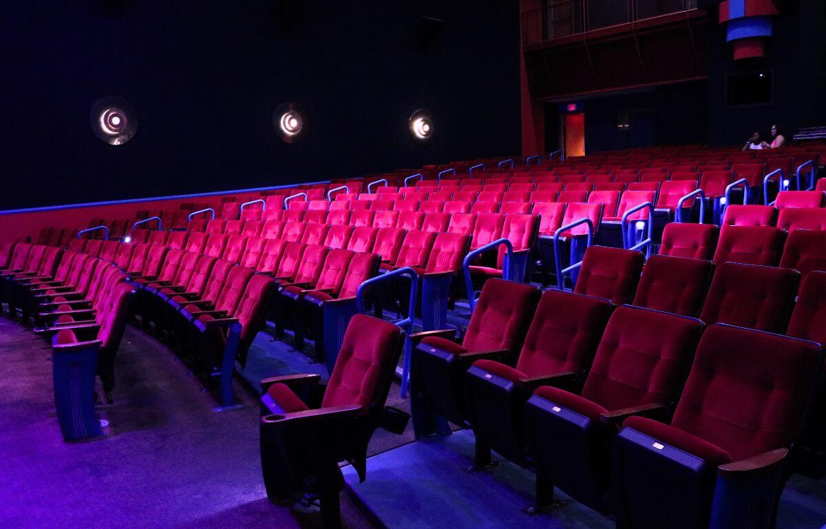 Rows of theatre seating with dim pink and magenta lighting. Two guests in Barbie-themed clothing sit in the back of the theatre waiting for a screening of Barbie to begin.