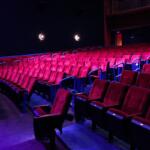 Rows of theatre seating with dim pink and magenta lighting. Two guests in Barbie-themed clothing sit in the back of the theatre waiting for a screening of Barbie to begin.