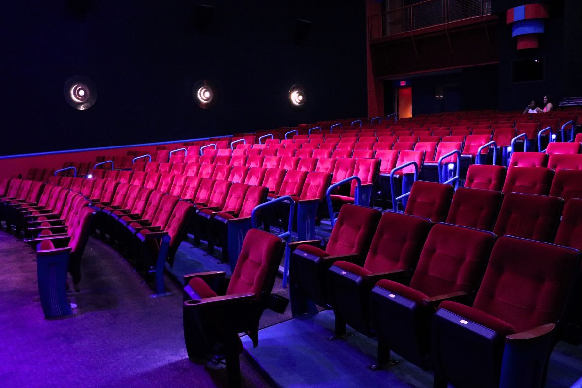 Rows of theatre seating with dim pink and magenta lighting. Two guests in Barbie-themed clothing sit in the back of the theatre waiting for a screening of Barbie to begin.