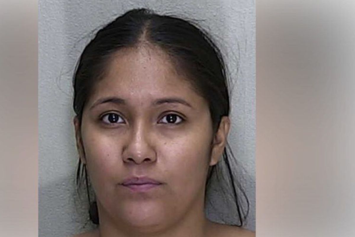 Gray wall in the background, face of a woman, with hair parted in the middle.