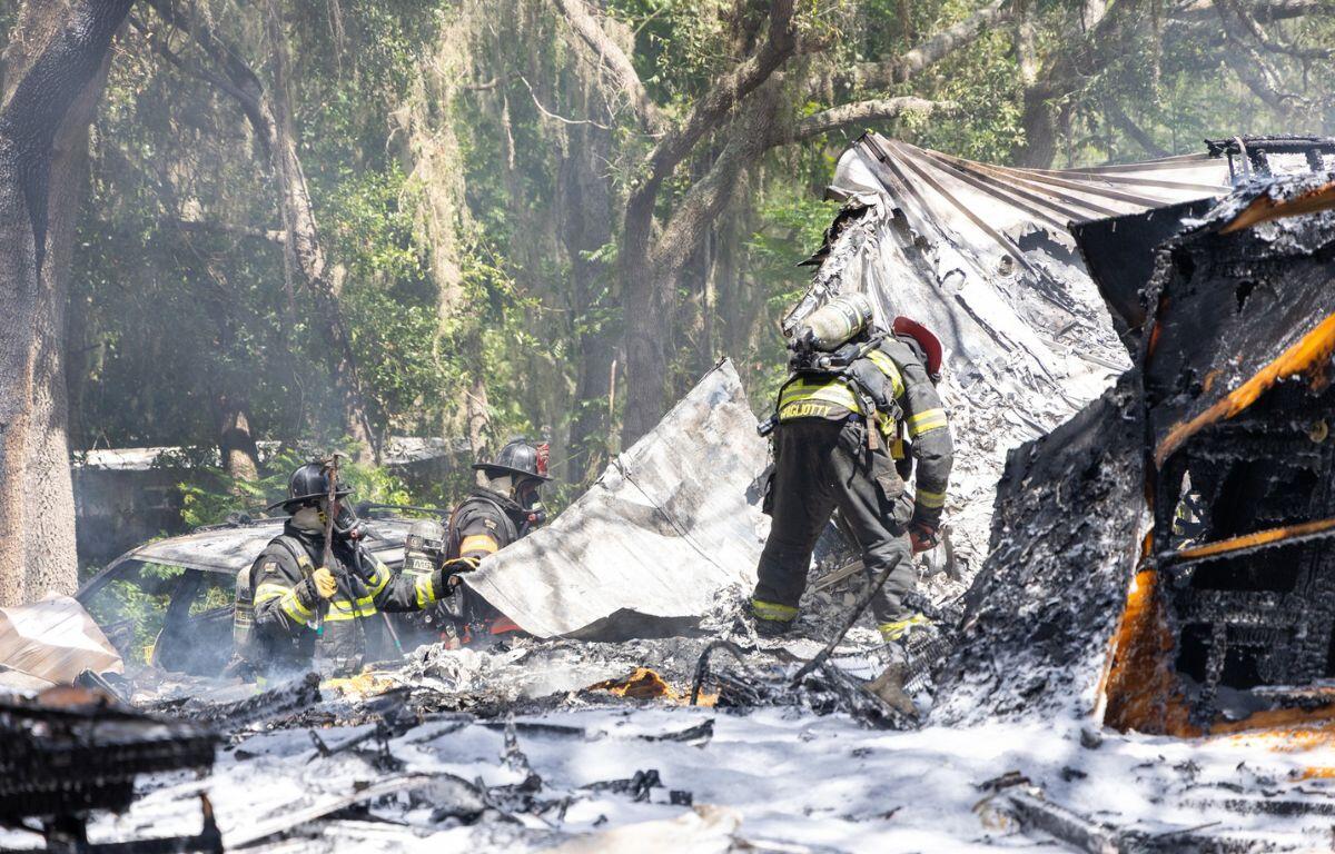 Firefighters assess the charred remains of a burnt structure, surrounded by ash and debris.