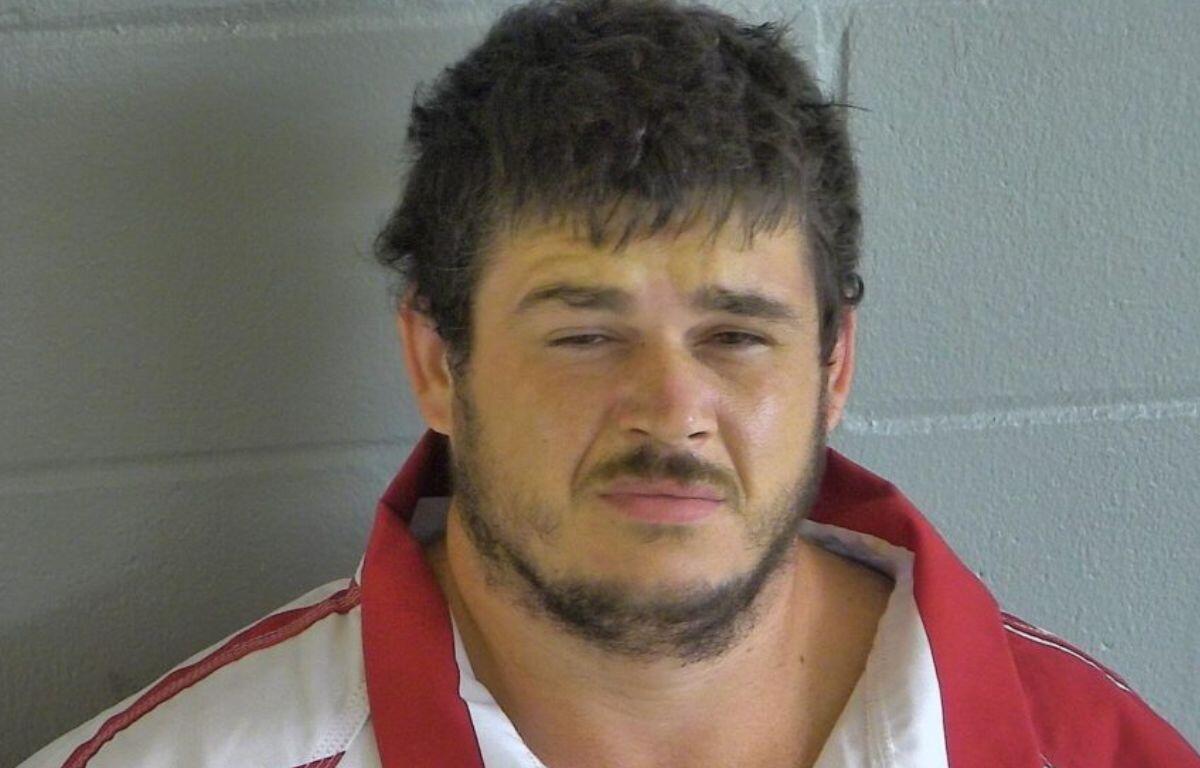 A man in an orange and white jump suit against a gray wall.